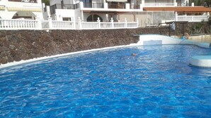 Ein Schwimmbecken mit klarem, blauem Wasser, umgeben von einem weißen Zaun und einer Steinmauer.