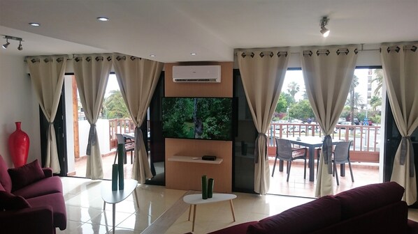 A modern living room with a flat-screen TV, a sofa, a coffee table, and a balcony with outdoor seating.