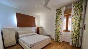 A bedroom with a bed, a dresser, a nightstand, a ceiling fan, and a window with curtains. - Apartment/ flat - Gavorrano (Gavorrano)