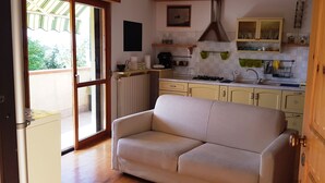 A compact kitchen with a sofa in the living area, a sliding glass door leading to a balcony, and a wooden door. - Apartment/ flat - Gavorrano (Gavorrano)