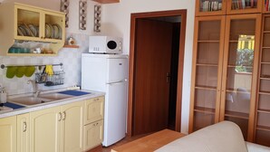 A compact kitchen with a stove, sink, and white refrigerator. There is a wooden door leading to another room and a bookshelf with books. - Apartment/ flat - Gavorrano (Gavorrano)