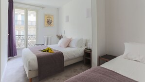 Et hotelværelse med en seng, et natbord, et vindue med gardiner, en radiator og et billede på væggen.