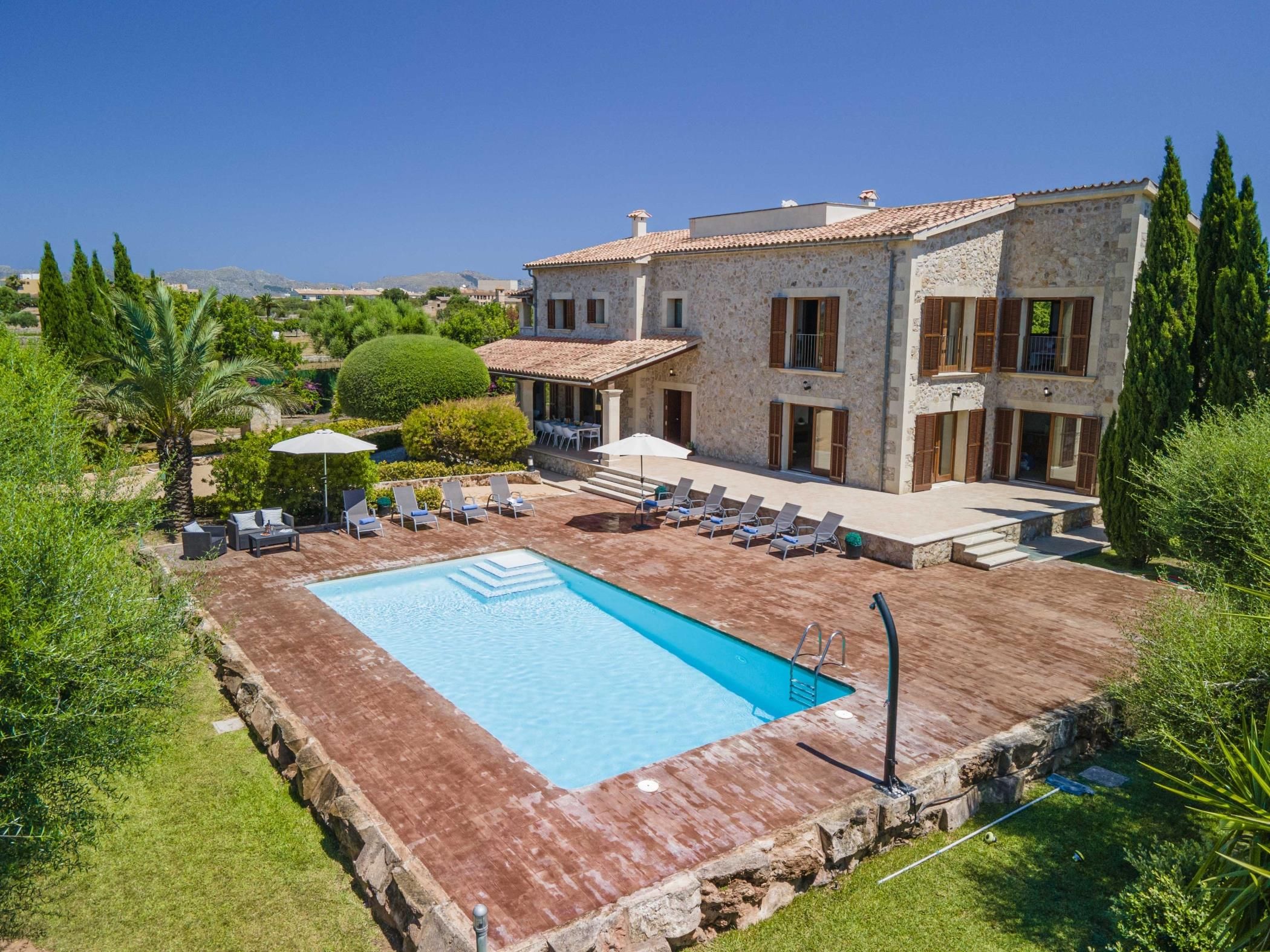 A villa with a swimming pool, outdoor seating, and a view of the surrounding landscape.