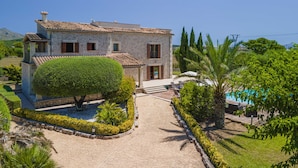 A two-story stone house with a tiled roof, a well-maintained garden with a large hedge, and a swimming pool. - Villa Santa Maria / finca Santa Maria (Alcúdia)