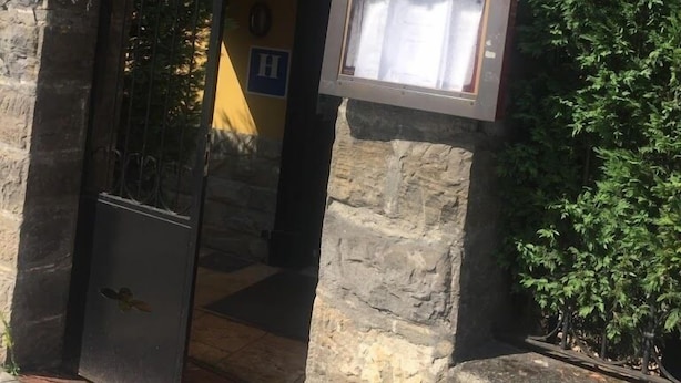 A stone archway with a 'MENU' sign above it, leading to a building with a yellow facade and a window with shutters. - Hotel Restaurante Aldama (Amurrio)