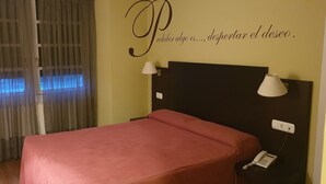 A hotel room with a bed, two bedside lamps, a telephone, and a wall with a motivational quote. - Hotel Restaurante Aldama (Amurrio)