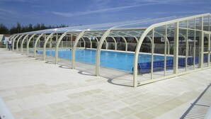 A swimming pool with a glass enclosure, surrounded by a tiled deck.
