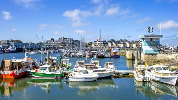 A marina with various boats docked, a prominent building with a flag, and a clear blue sky.