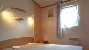 A room with a bed, a nightstand, a lamp, and a window with curtains.