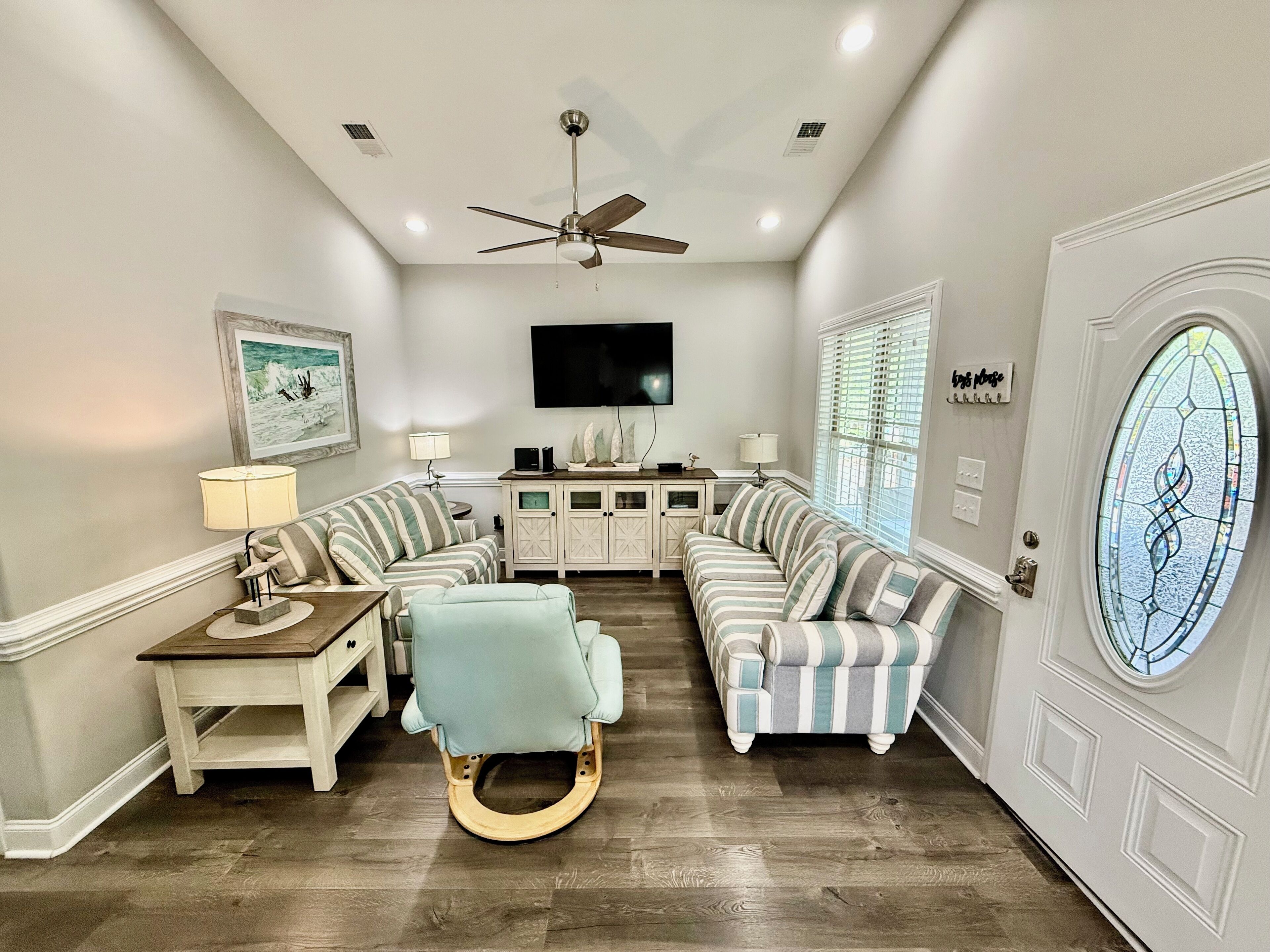 A living room with a sectional sofa, a rocking chair, a television, and a ceiling fan.