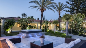 Un patio exterior con una zona de estar, un jacuzzi y un sendero bien iluminado que lleva a un edificio.