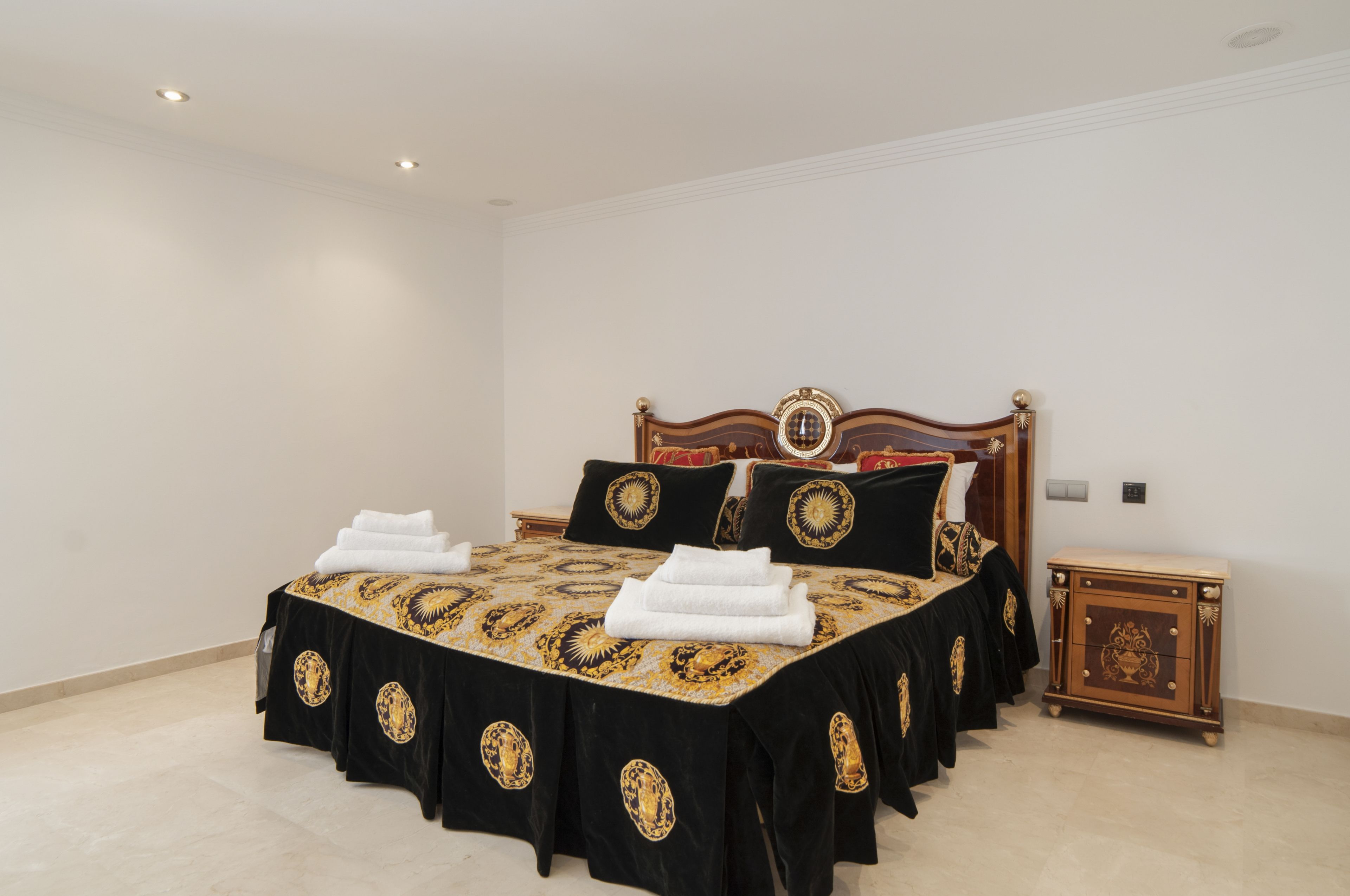Un lit bien fait, recouvert d’une couvre-lit noire et dorée, avec une tête de lit en bois et une petite table de chevet en bois dotée de tiroirs.