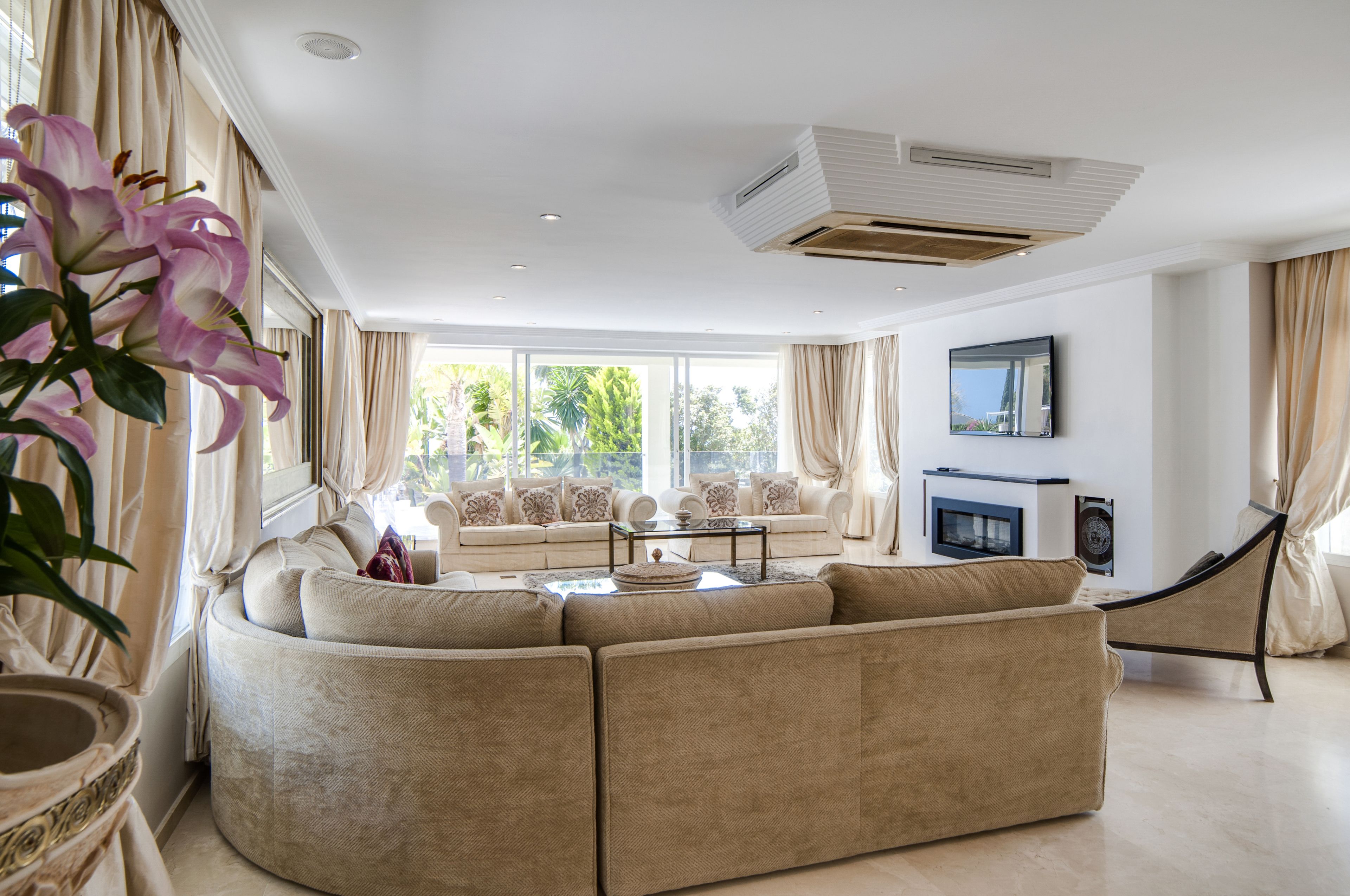 A spacious living room with a large beige sectional sofa, a coffee table, and a flat-screen TV mounted on the wall.