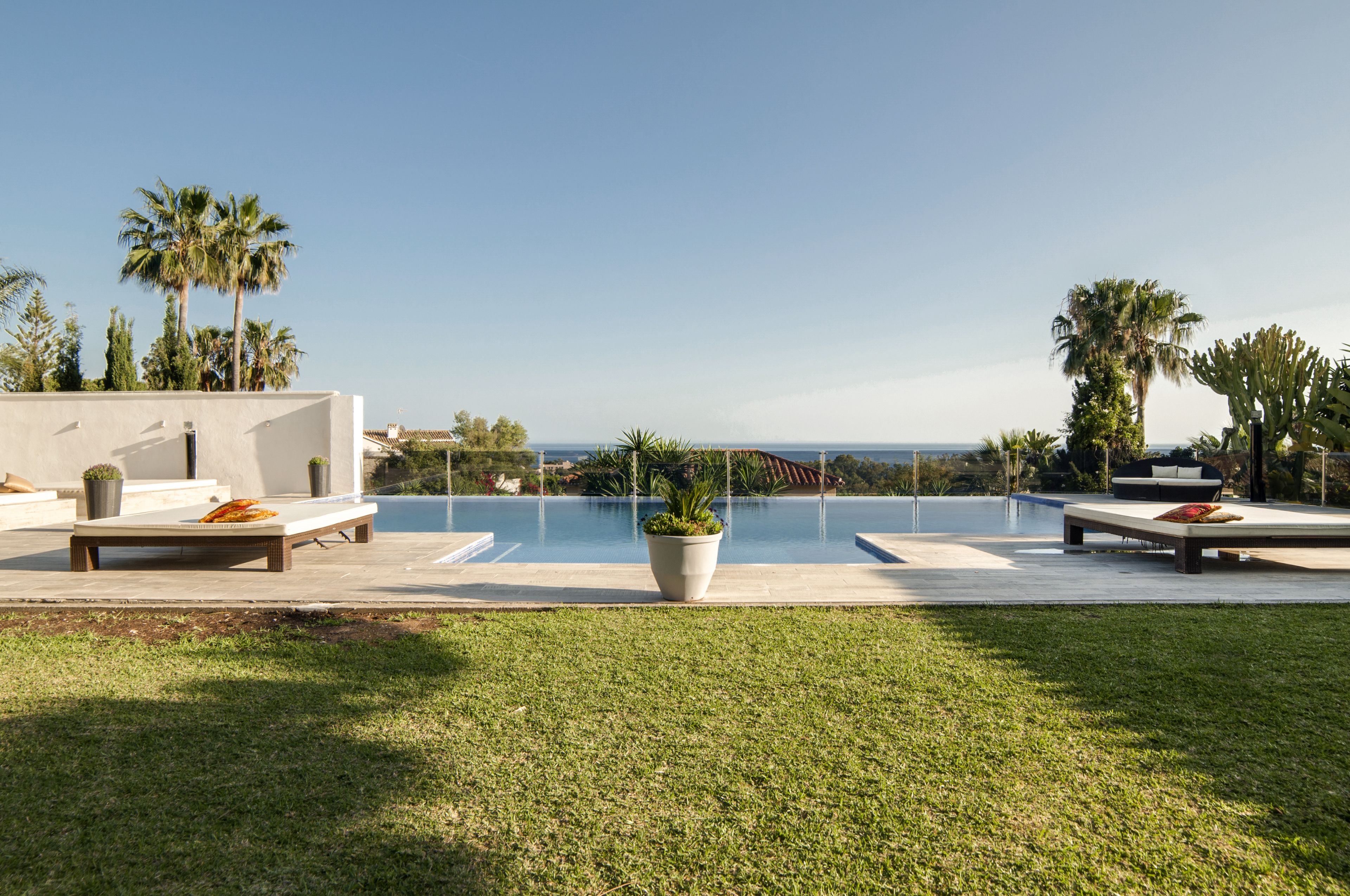A modern outdoor pool area with seating and palm trees, overlooking a clear view of the ocean.