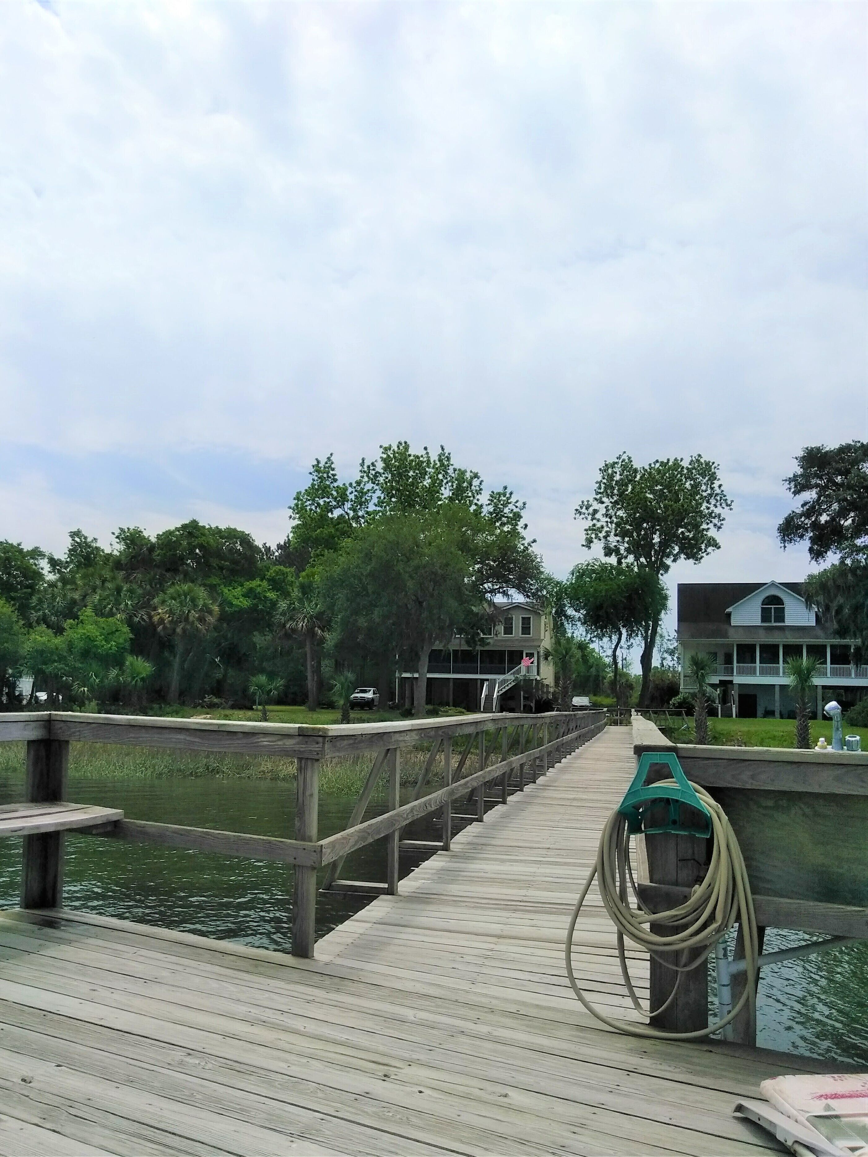 A wooden dock extending over water with a house in the background.