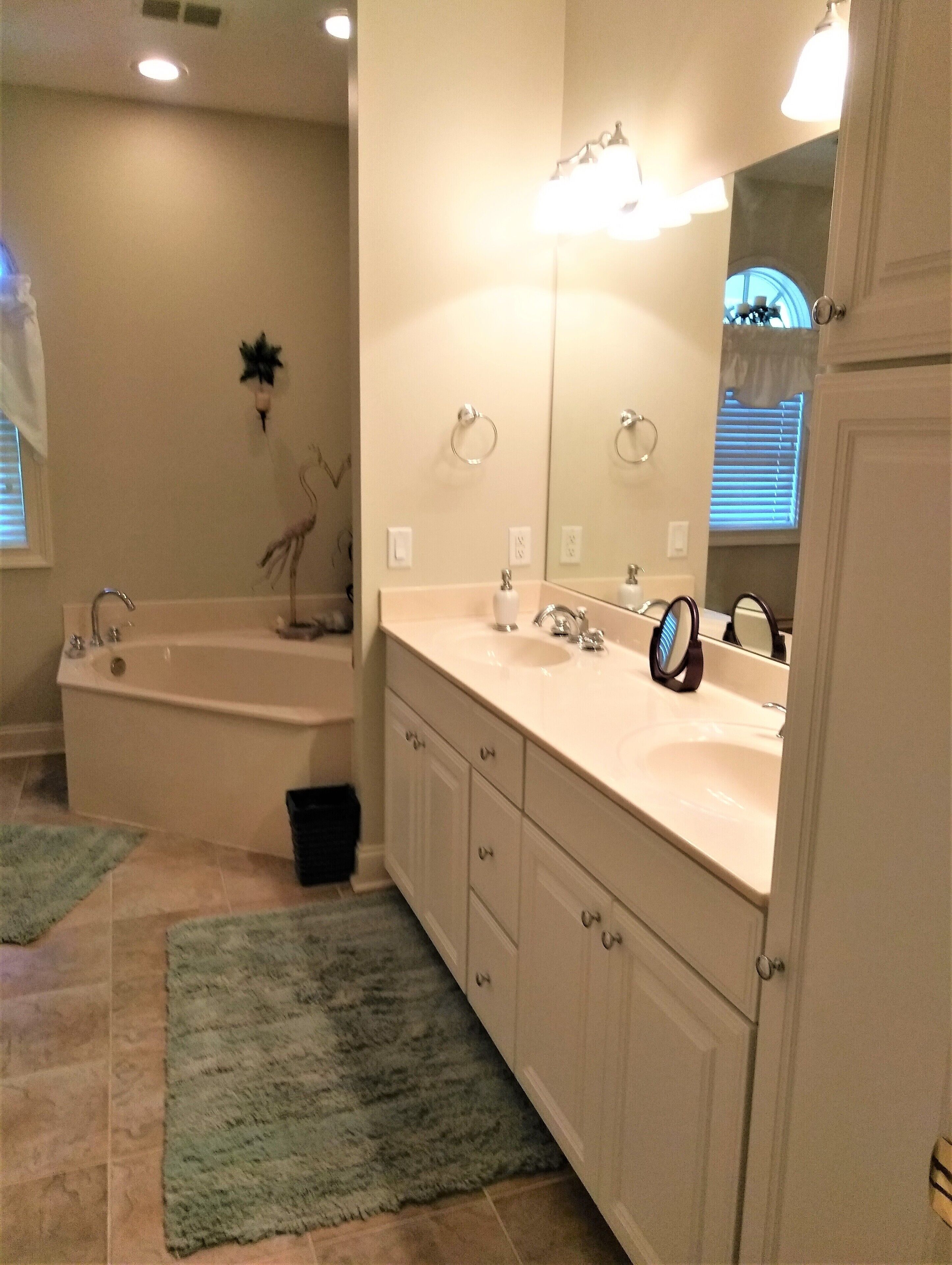 A bathroom with a bathtub, two sinks, a large mirror, and a small trash bin.