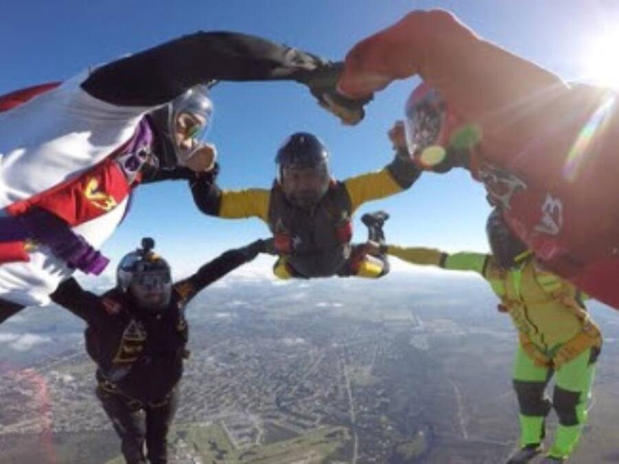 Three skydivers in mid-air with parachutes, one wearing a white and red flag, another in yellow and black, and the third in black and red.