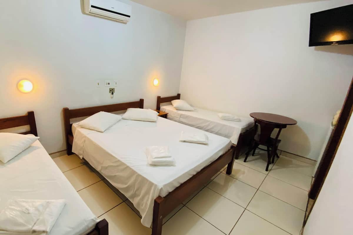 Ein Hotelzimmer mit drei Einzelbetten, einem kleinen runden Tisch und einem an der Wand befestigten Fernseher.