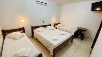 A hotel room with three single beds, a small round table, and a TV mounted on the wall.