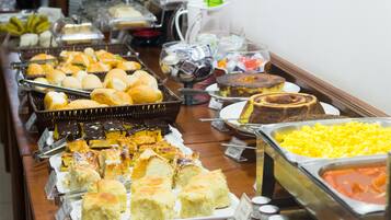 Buffet com diversos alimentos, incluindo pães, doces e uma variedade de sobremesas.