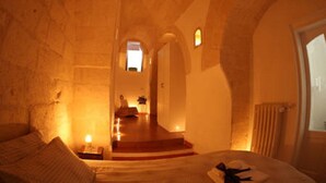 Una habitación tenuemente iluminada con una cama, una mesita y una silla. Se ve una ventana con vistas a una escalera que conduce a una puerta.