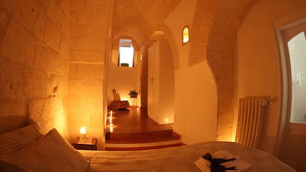 A dimly lit room with a bed, a small table, and a chair. There is a window with a view of a staircase leading to a door. - Holiday home L'Alloro with private parking - MATERA (Matera)