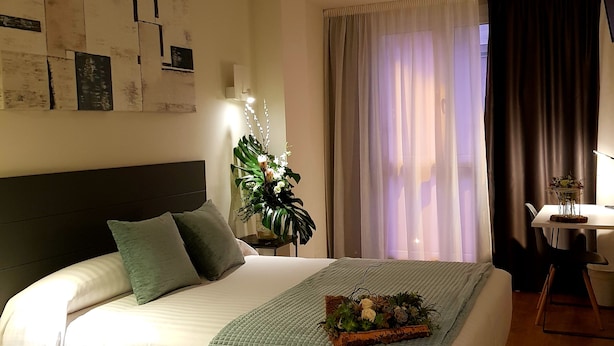Un dormitorio ordenado con cama, mesita de noche, lámpara y una planta decorativa.
