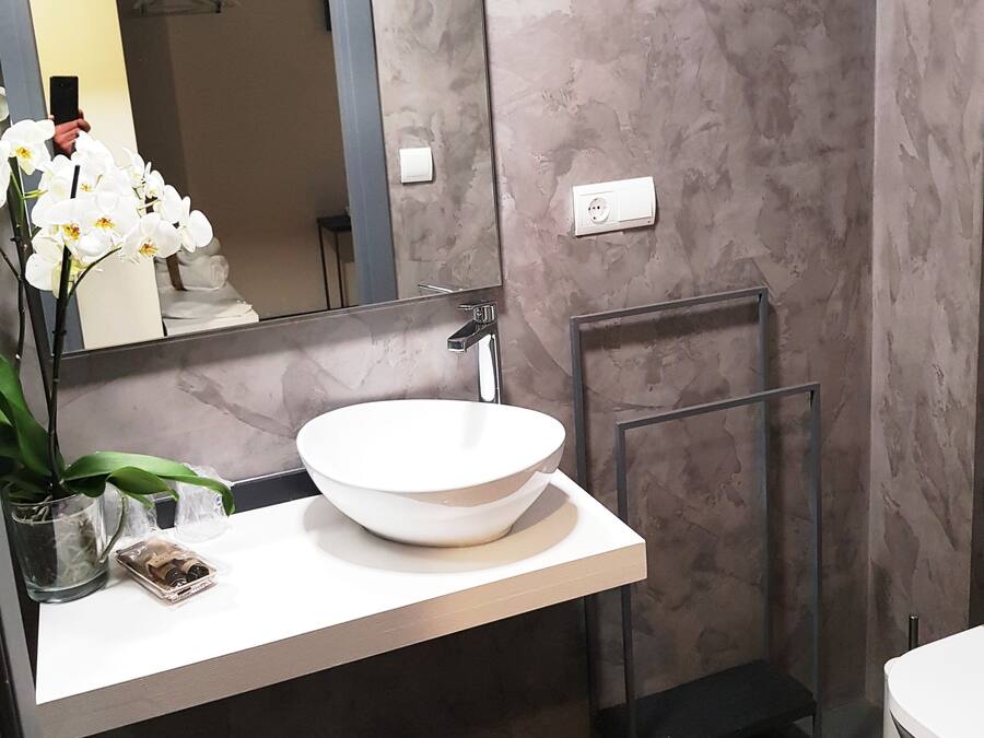 Un baño moderno con un lavamanos grande y blanco, un espejo, un perchero y una pequeña orquídea en maceta.