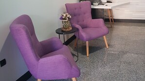 Una habitación moderna con dos sillones morados, una mesita redonda con un jarrón de flores y un escritorio con una computadora.