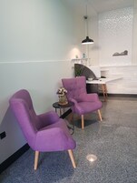 Una habitación moderna con dos sillones morados, una mesita redonda con un jarrón de flores y un escritorio con una computadora.
