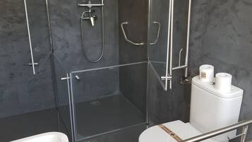 A modern bathroom with a walk-in shower, a toilet with a safety rail, and a bathtub.
