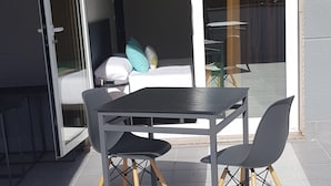 Un patio exterior moderno con una mesa y sillas, una puerta corrediza de vidrio que da a un balcón y un piso de baldosas.