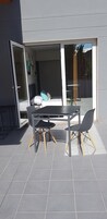 Un patio exterior moderno con una mesa y sillas, una puerta corrediza de vidrio que da a un balcón y un piso de baldosas.