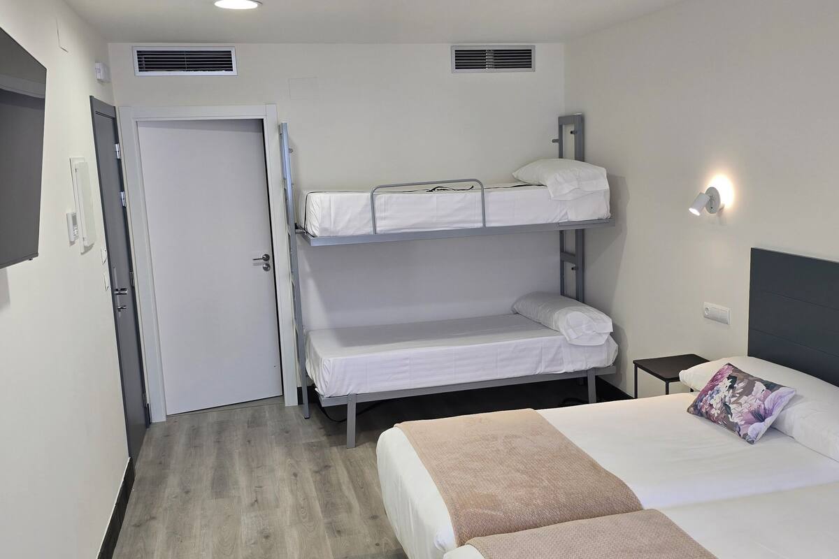 Une chambre d’hôtel avec des lits superposés, un téléviseur à écran plat, une table de chevet et un lit agrémenté d’oreillers à motifs floraux.