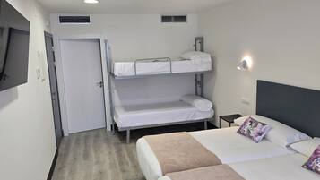 Et hotelværelse med køjesenge, et fladskærms-TV, et sengebord og en seng med blomstermønstrede puder.
