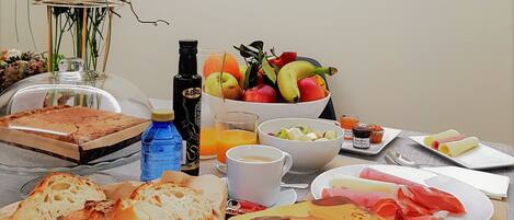 Una mesa de desayuno con pan, fruta, jugo y una taza de café.