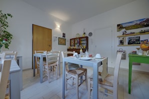 A dining area with a wooden table and chairs, a green side table, and a cabinet with various items. - La Malvasia (Trento)