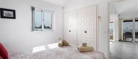 A bedroom with a bed, a window, a wardrobe, and a view of the outside.