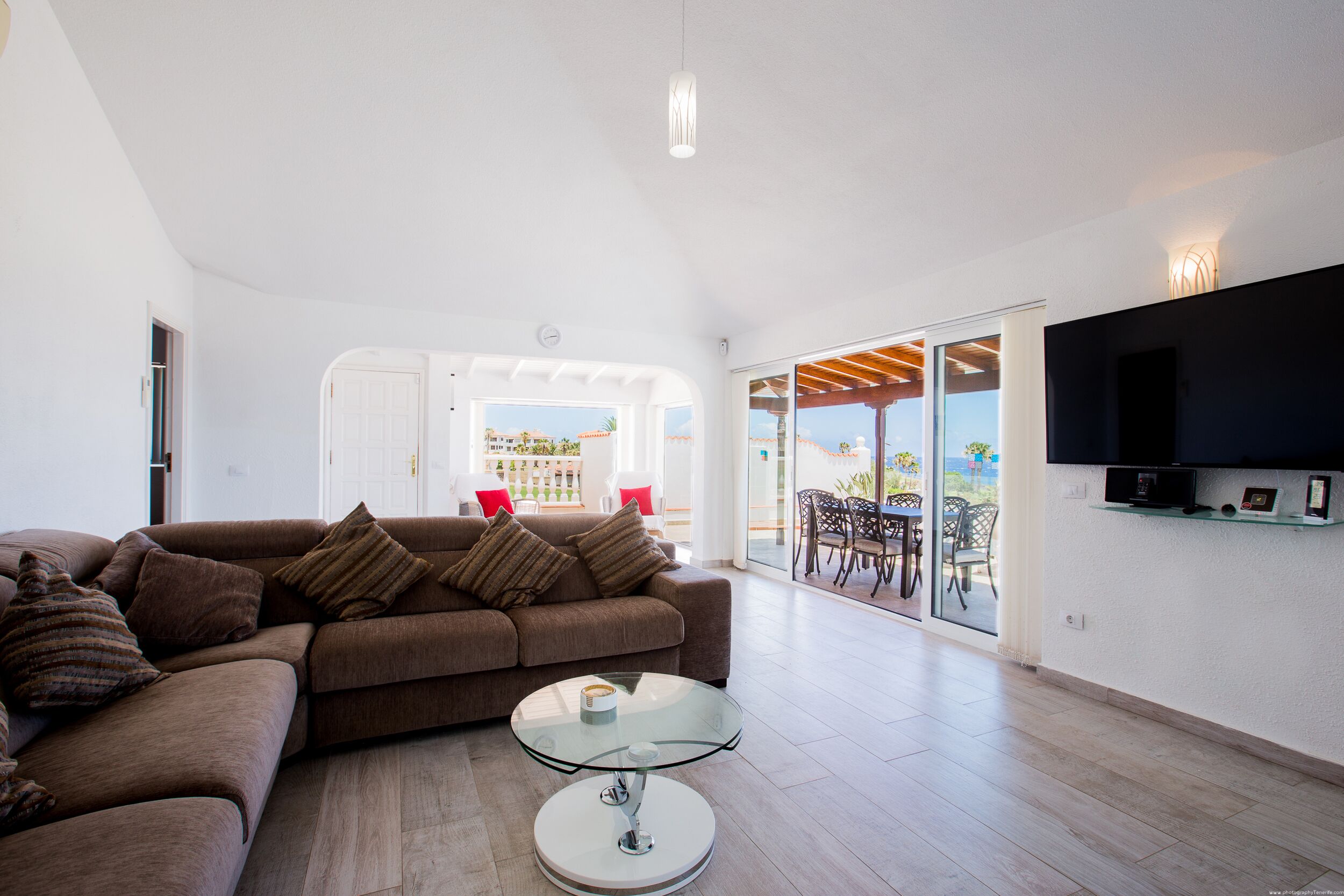 Una sala de estar moderna con un sofá marrón, una mesa de centro de cristal y un televisor de pantalla plana montado en la pared.
