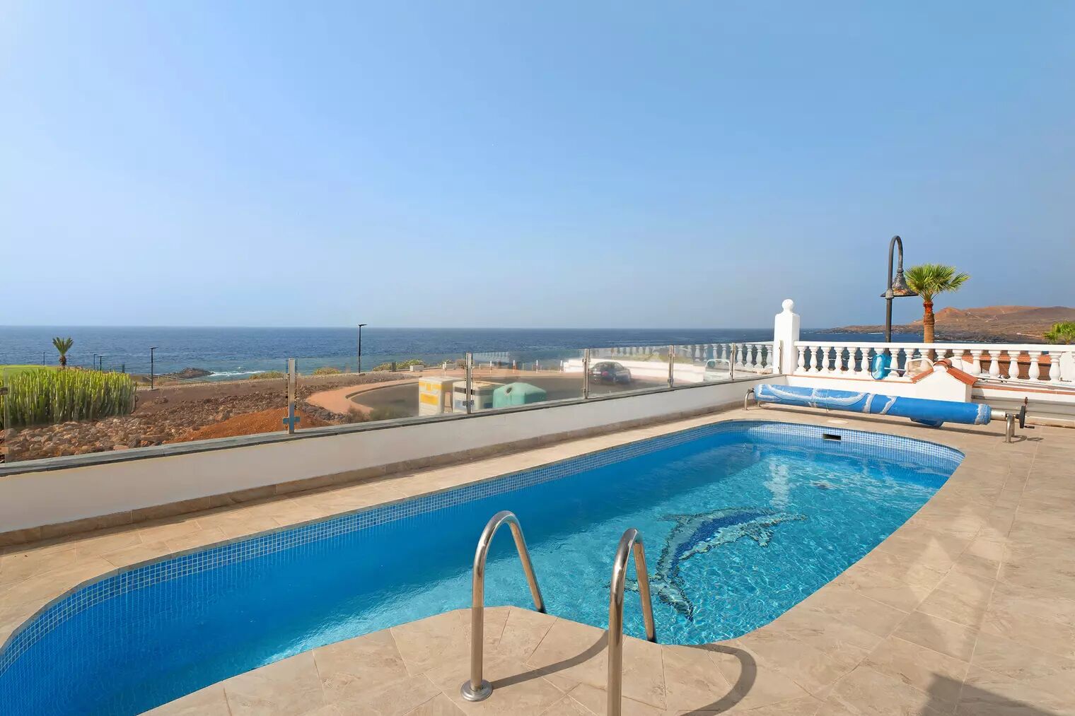 Una piscina con vistas al océano, un edificio blanco y una palmera.