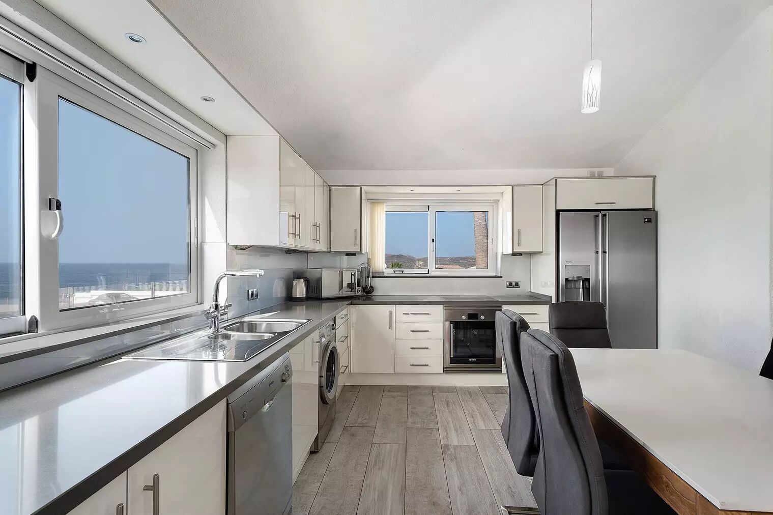 Una cocina moderna con un amplio ventanal, electrodomésticos de acero inoxidable y vista al mar.