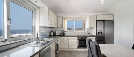 Una cocina moderna con un amplio ventanal, electrodomésticos de acero inoxidable y vista al mar.