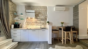 A compact kitchen with white cabinets, a stone accent wall, and a small dining area with two chairs. - Apartments & Rooms Dujam (Split)
