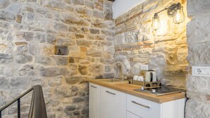 A stone-walled kitchen with a wooden countertop, white cabinets, and a built-in stove. - Apartments & Rooms Dujam (Split)