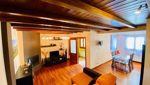 A spacious living area with a wooden ceiling, a black entertainment unit, and a dining area with a glass table and chairs. - House Forn for 6 people (Sort)