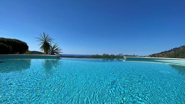 En vacker, turkosblå infinitypool med utsikt över havet och de avlägsna kullarna.