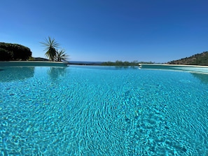 Ein klarer, blauer Infinity-Pool mit Blick auf das Meer und sanfte Hügel in der Ferne.