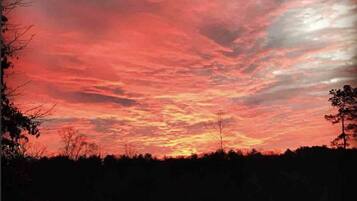 A sunset over a rural landscape with a fence and trees.