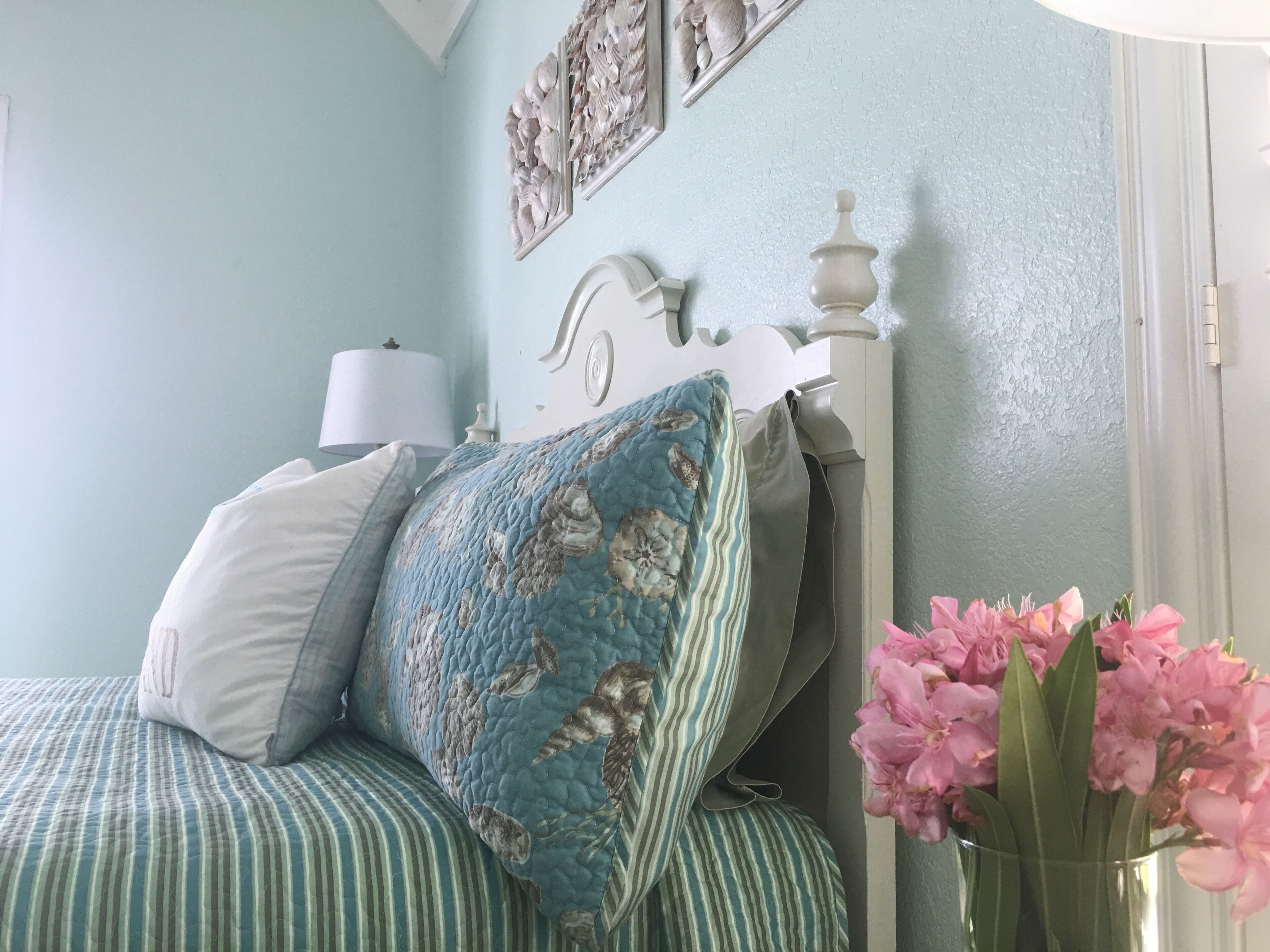 Een slaapkamer met een bed, kussens, een lamp en een vaas met bloemen.