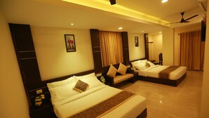 A hotel room with two beds, a ceiling fan, and a nightstand with a vase of flowers. - The Crescent Suites (Kanayannur)